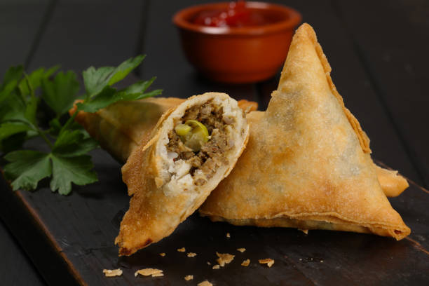 Chicken samosa broken open to show the spiced filling, with dipping sauce behind