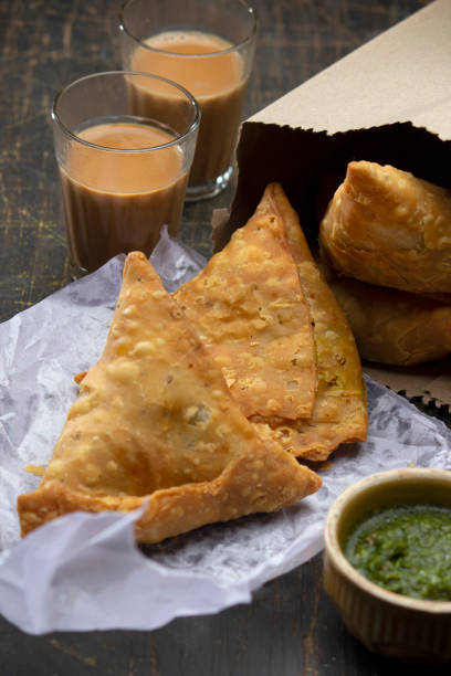 Freshly fried samosas on paper with green chutney and two glasses of masala chai